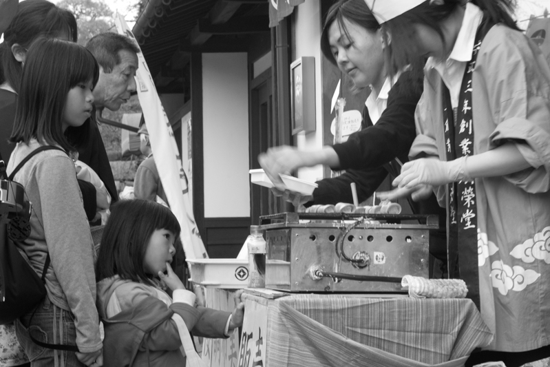 Two girls waiting as the shop staff prepares a batchof pancake-roll sweets (調布巻).